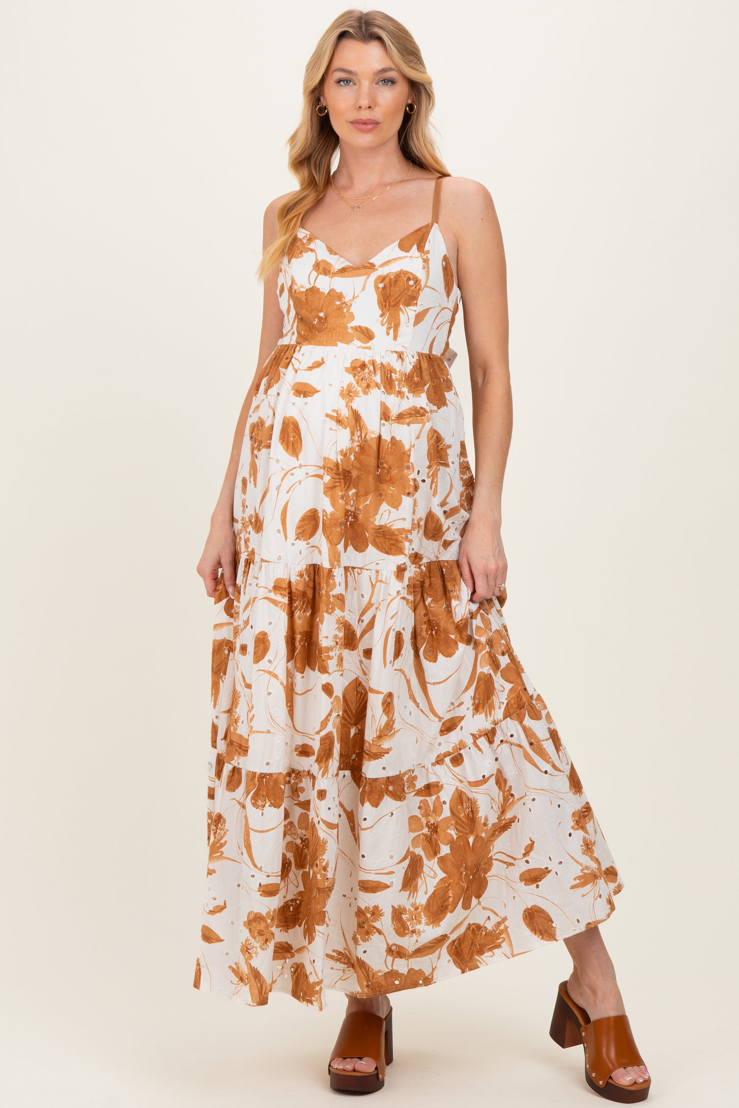 woman wearing a white maternity maxi dress with orange floral print and holding her baby bump
