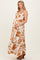 woman wearing a white and rust floral maternity maxi dress, gently cradling her baby bump