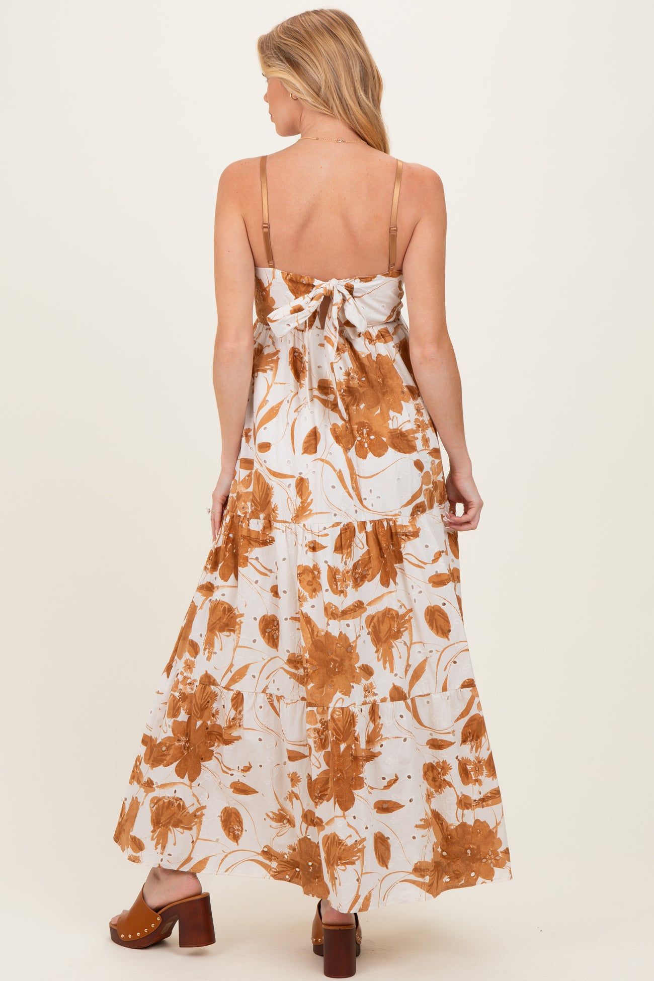 woman wearing a maternity maxi dress with a floral print in brown and white, showing a tied back detail and flowing skirt