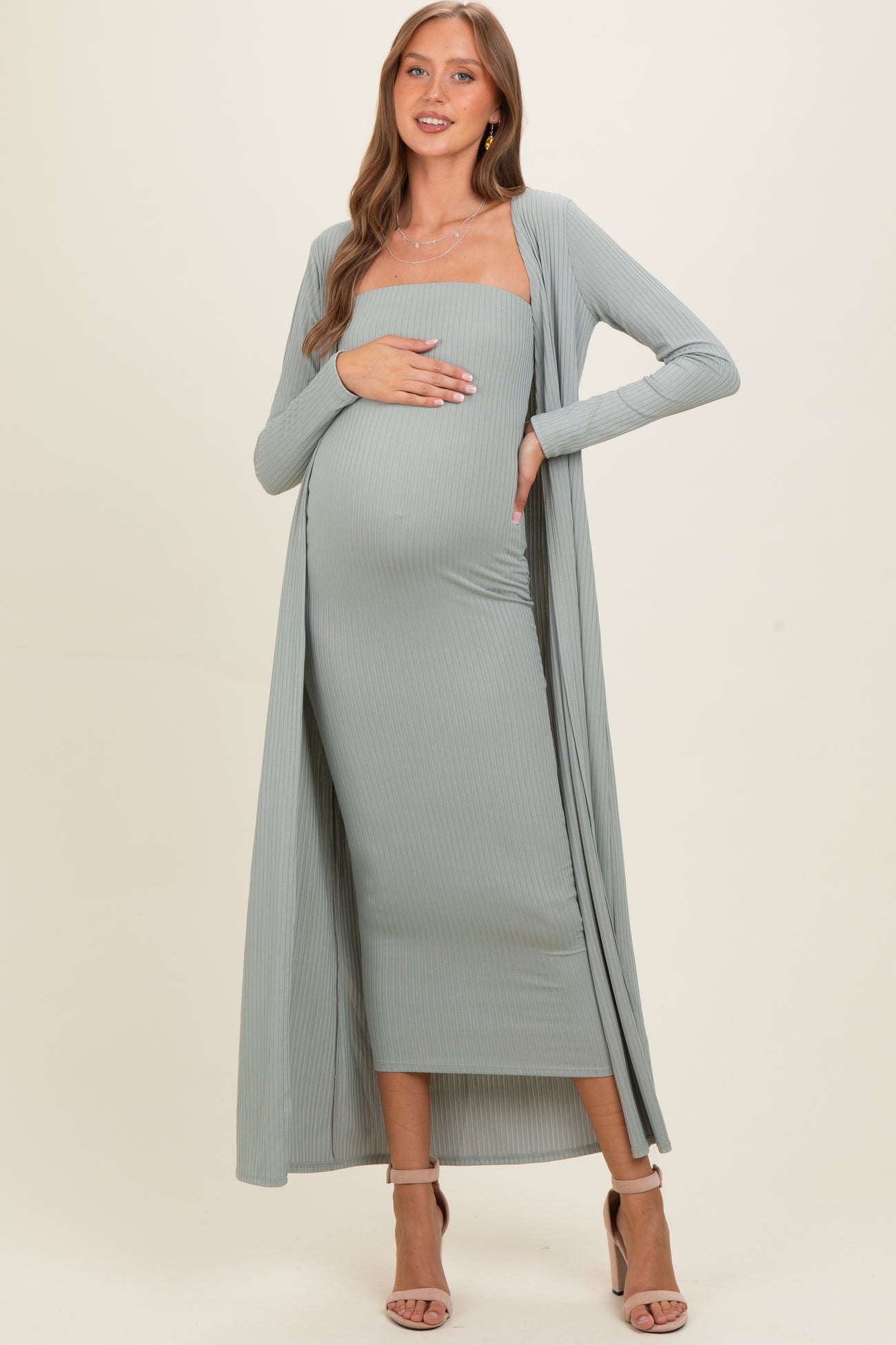 woman wearing a light green maternity dress with a matching long cardigan and holding her baby bump