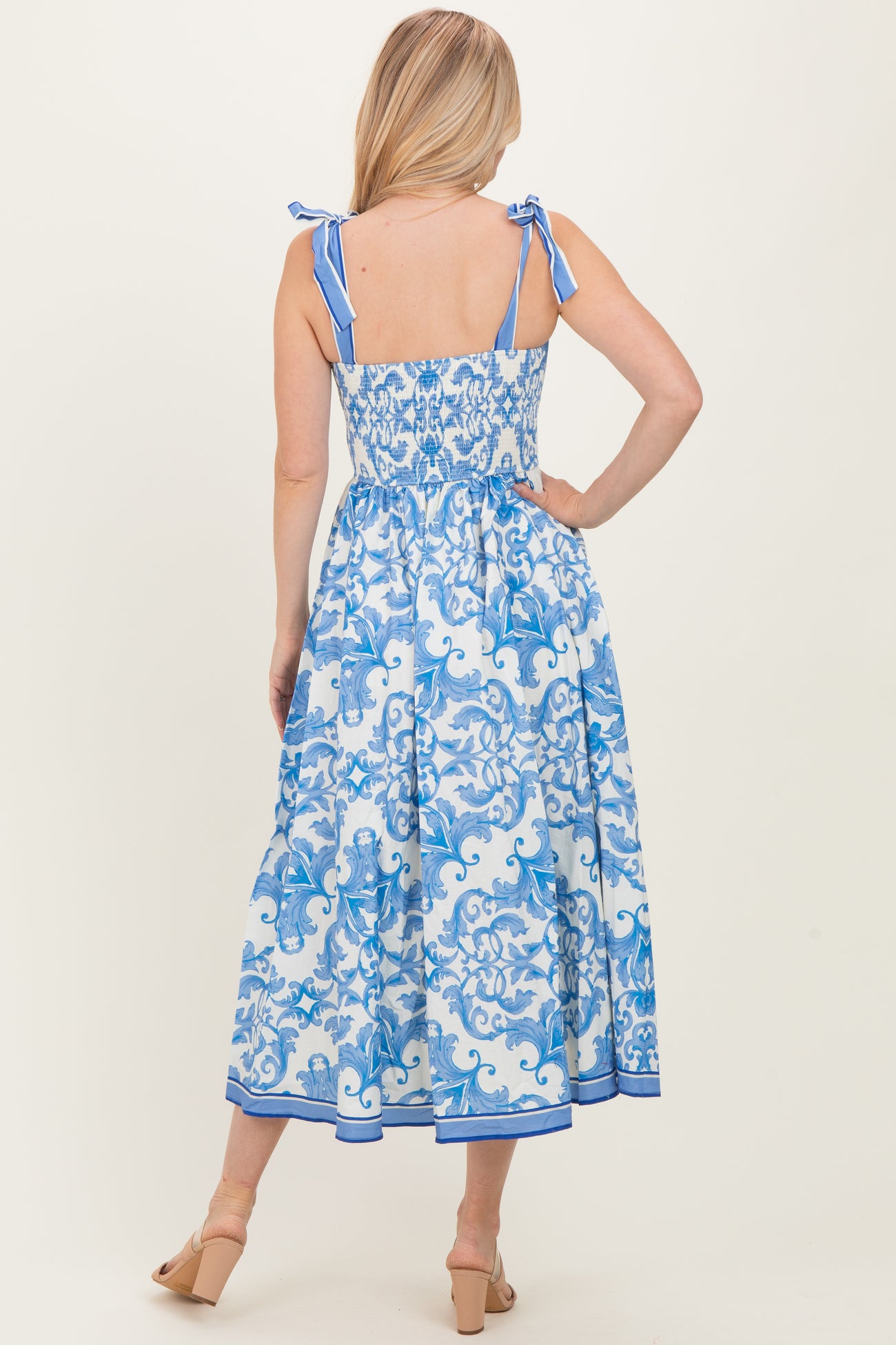 woman wearing a blue and white patterned midi dress with adjustable tie straps and a smocked back