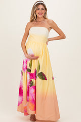 woman wearing a strapless yellow maternity maxi dress with pink floral prints and holding her baby bump
