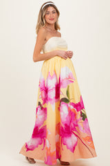 woman wearing a strapless yellow floral maternity gown with pink flowers and a flowing skirt, baby bump visible