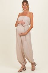 woman wearing a beige strapless maternity jumpsuit with a cinched waist and holding her baby bump