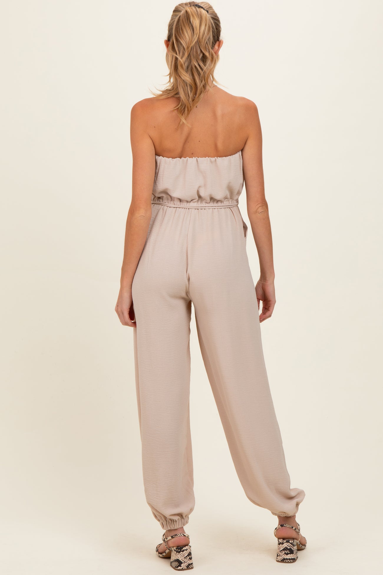 woman wearing a light beige strapless maternity jumpsuit with a gathered waistband and relaxed fit pants
