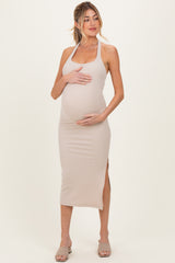 woman wearing a fitted beige ribbed maternity dress with side slits and holding her baby bump