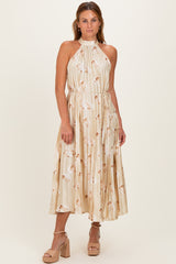 woman wearing a beige pleated halter neck dress with a floral print and a tied waist detail