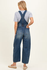 woman wearing a dark wash denim maternity overall with a loose fit and crossed back straps, showing a casual style