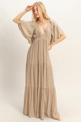 woman wearing a beige maxi dress with a deep v-neck and flowing sleeves, posing gracefully
