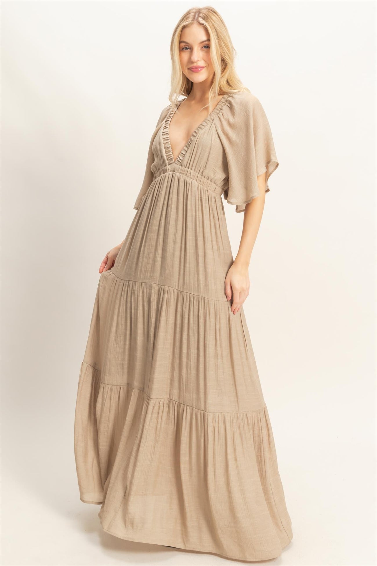 woman wearing a light beige maxi dress with flutter sleeves and deep v-neckline
