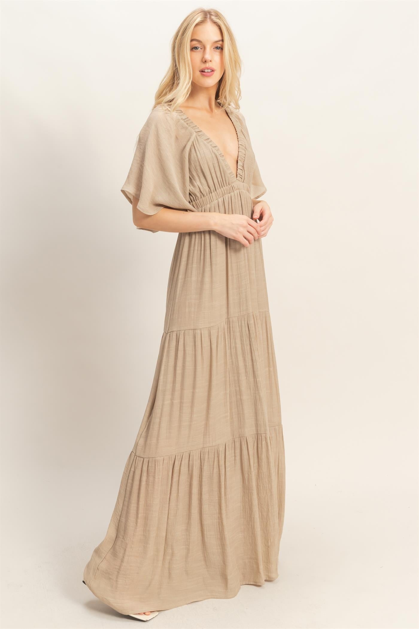 woman wearing a beige maxi dress with a deep v-neck and tiered skirt panels
