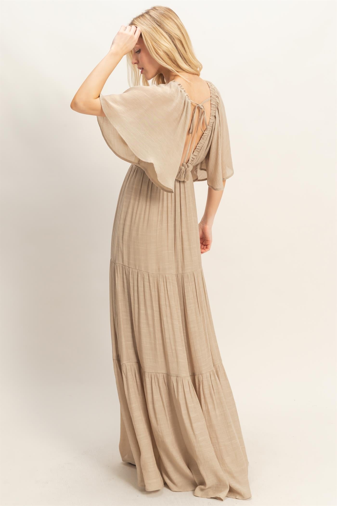 woman wearing a beige maxi dress with a tiered skirt and open back detail
