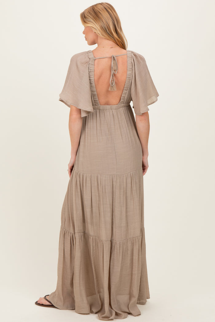 woman wearing a beige maternity maxi dress with short flutter sleeves and open back design