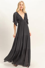woman wearing a black maxi dress with flutter sleeves and a deep v-neck, featuring a tiered skirt design