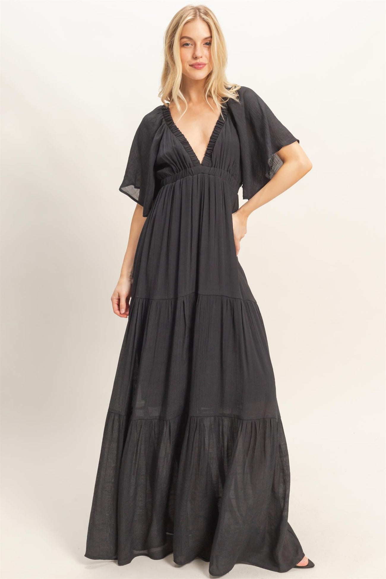 woman wearing a black tiered maxi dress with a deep v-neck and flutter sleeves