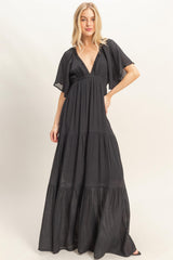 woman wearing a black tiered maxi dress with a deep v-neck and flutter sleeves