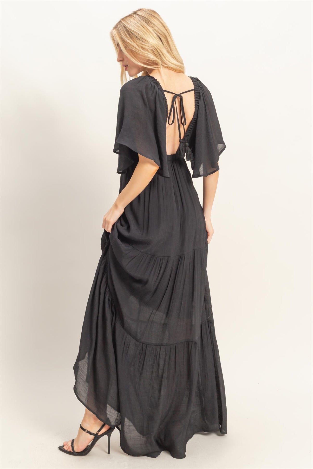 woman wearing a black maxi dress with flutter sleeves and an open back, showcasing a flowing tiered design