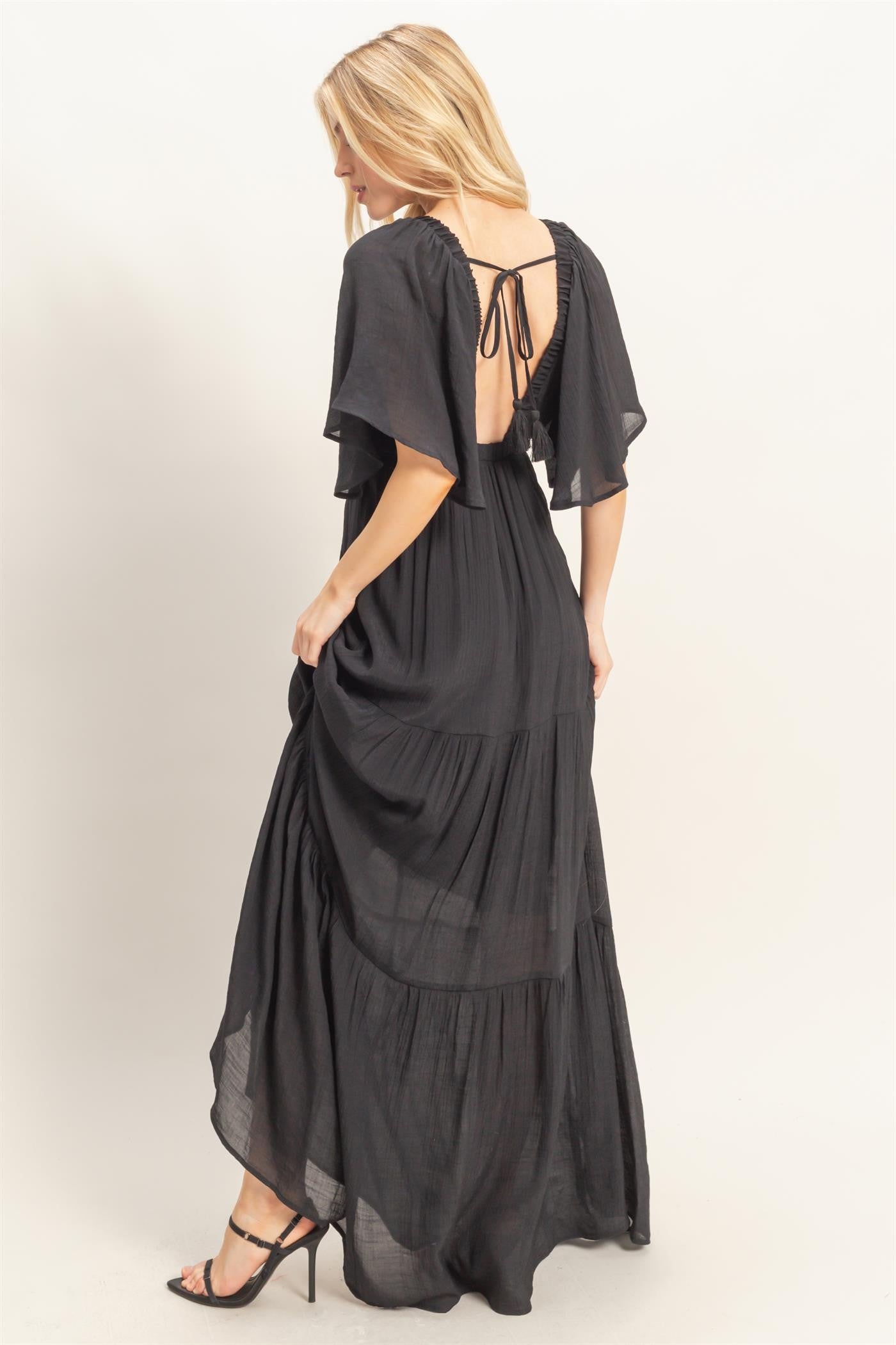 woman wearing a black maxi dress with flutter sleeves and an open back, showcasing a flowing tiered design