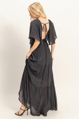 woman wearing a black maxi dress with flutter sleeves and an open back, showcasing a flowing tiered design