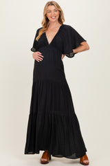 woman wearing a black maternity maxi dress with a deep V-neck and flutter sleeves, showing her baby bump