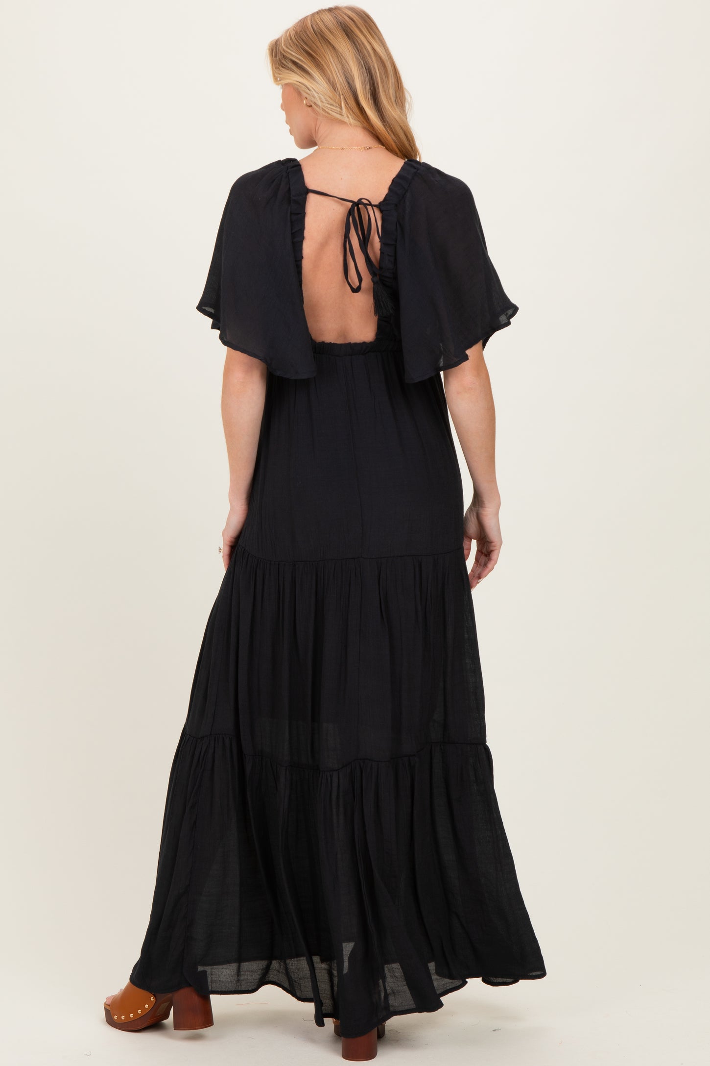 woman wearing a black tiered maxi dress with flutter sleeves and an open back, showcasing maternity wear style