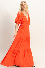 woman wearing a vibrant orange maxi dress with a deep v-neck and tiered skirt, posing against a light background