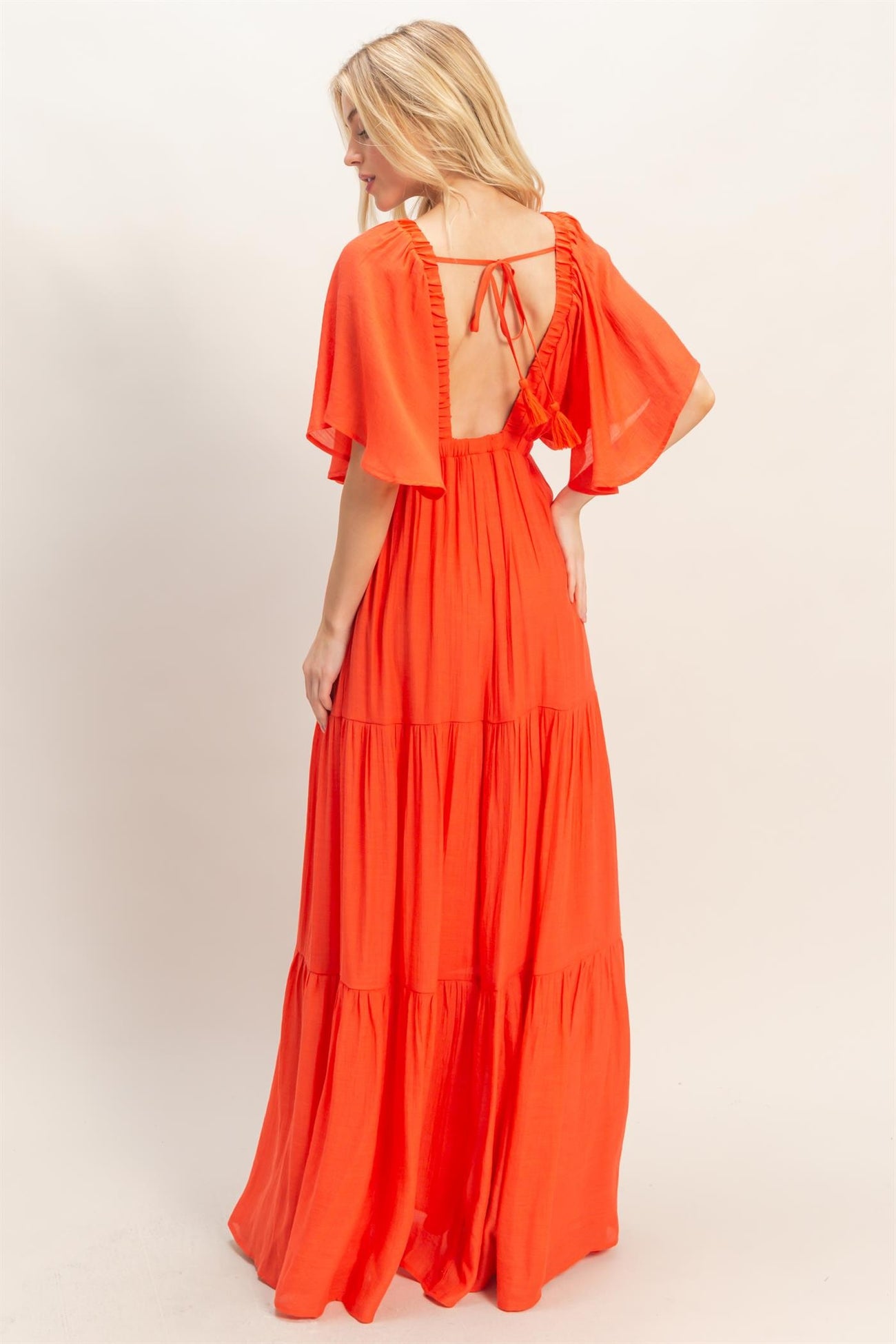 woman wearing a bright orange maxi dress with flutter sleeves and an open back, displayed from the back