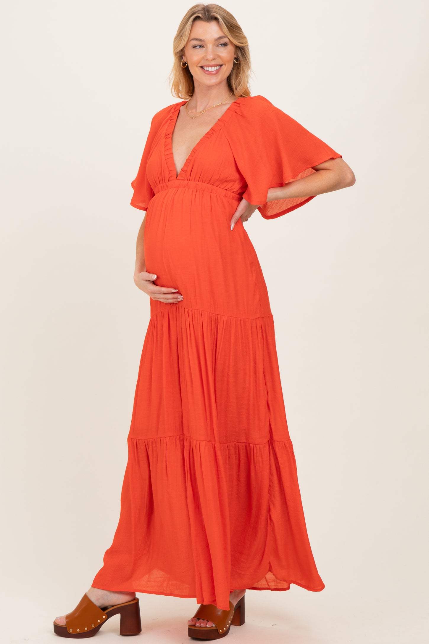woman wearing a vibrant orange maternity maxi dress with flutter sleeves and a baby bump visible