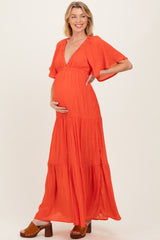 woman wearing a vibrant orange maternity maxi dress with flutter sleeves and a baby bump visible
