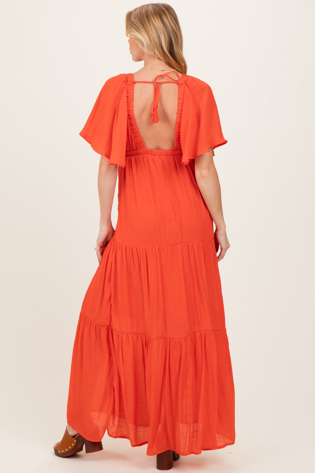 woman wearing a bright orange maternity maxi dress with flutter sleeves and a tie-back detail
