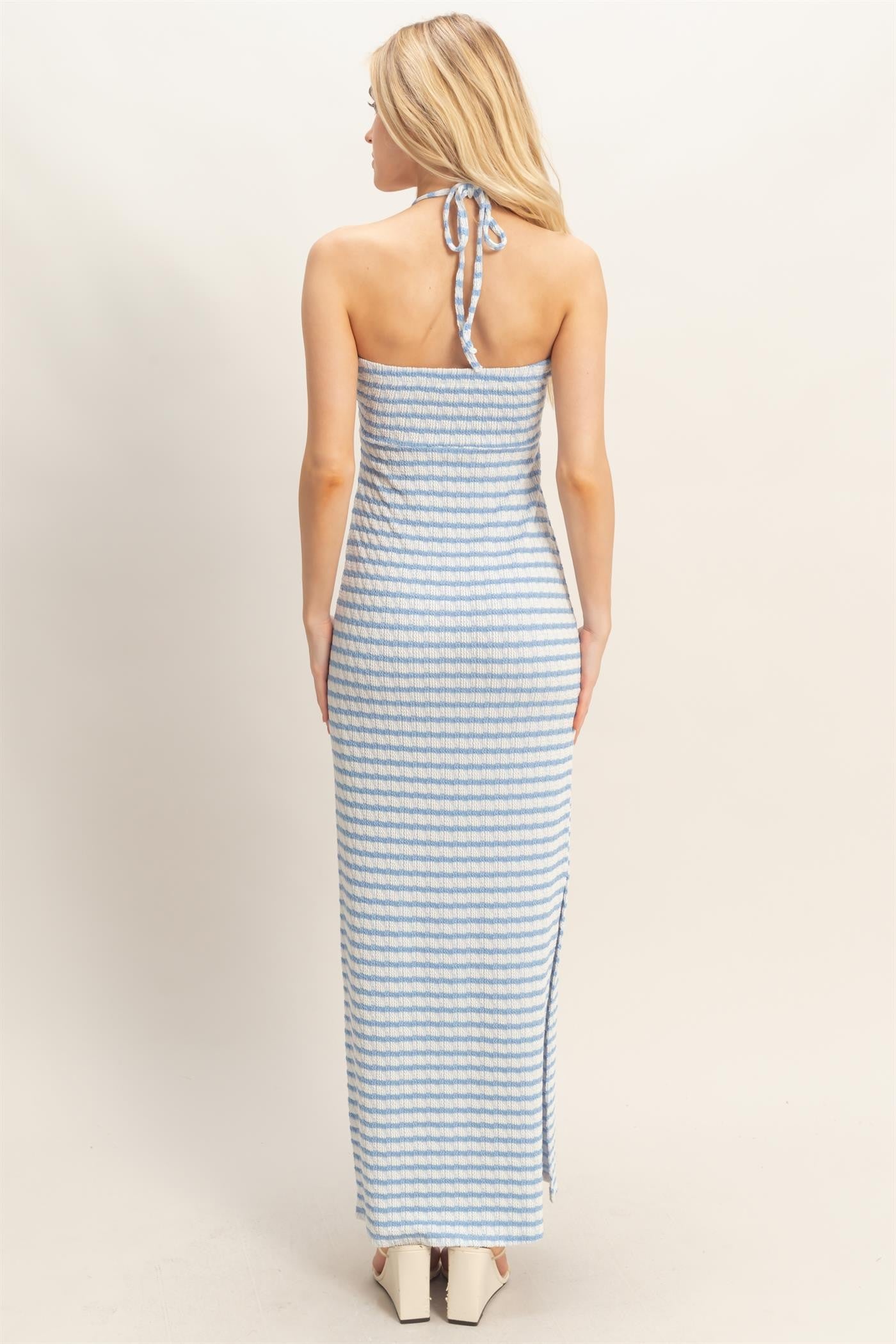 woman wearing a backless light blue and white striped maxi dress with a halter neck tie