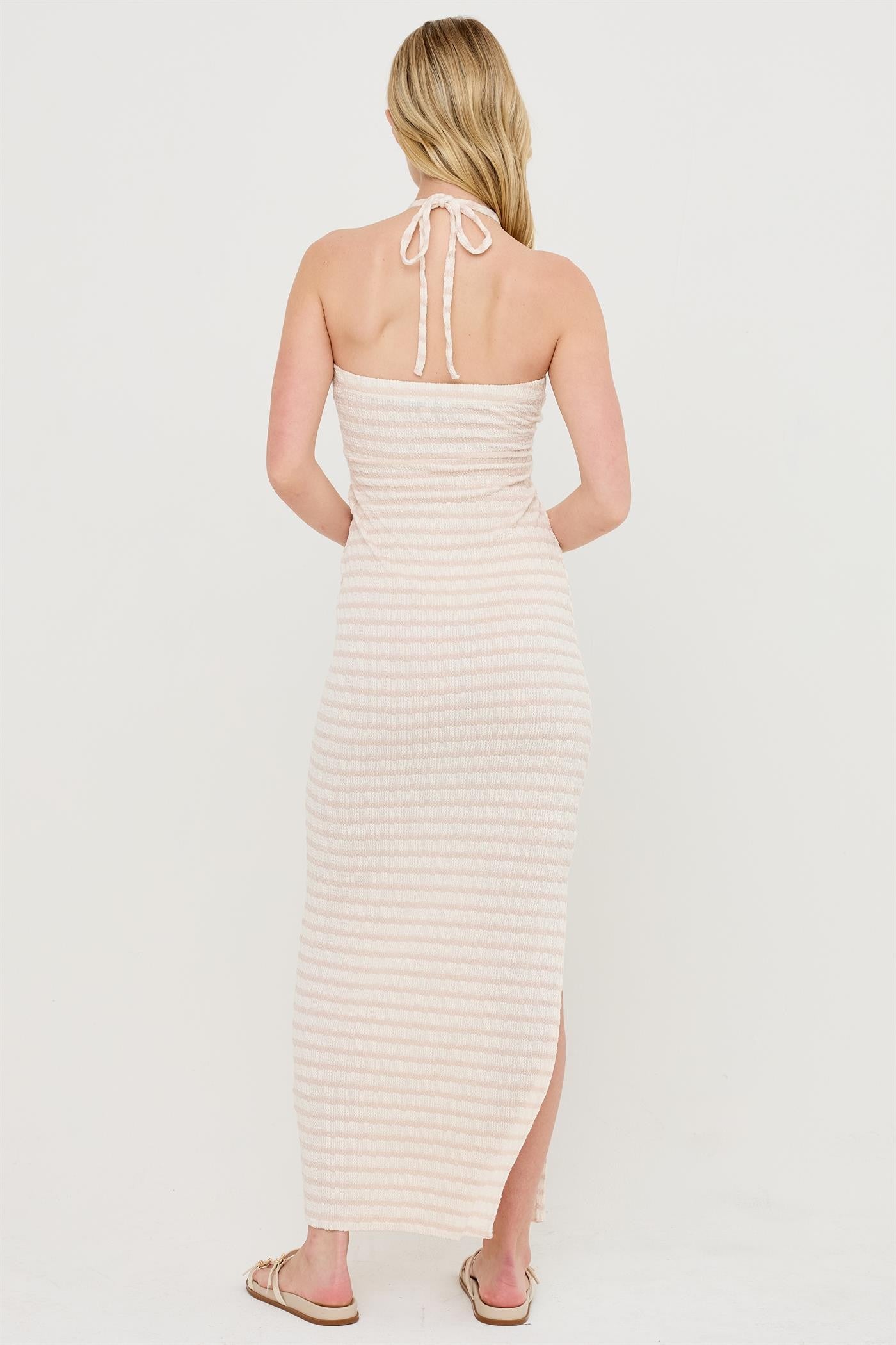 woman wearing a light pink striped maxi dress with a halter neckline and a thigh-high slit