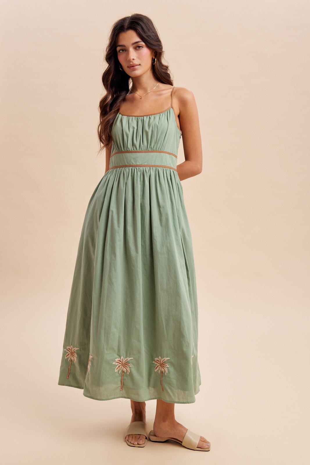 woman wearing a light green maxi dress with embroidered palm tree details and adjustable spaghetti straps