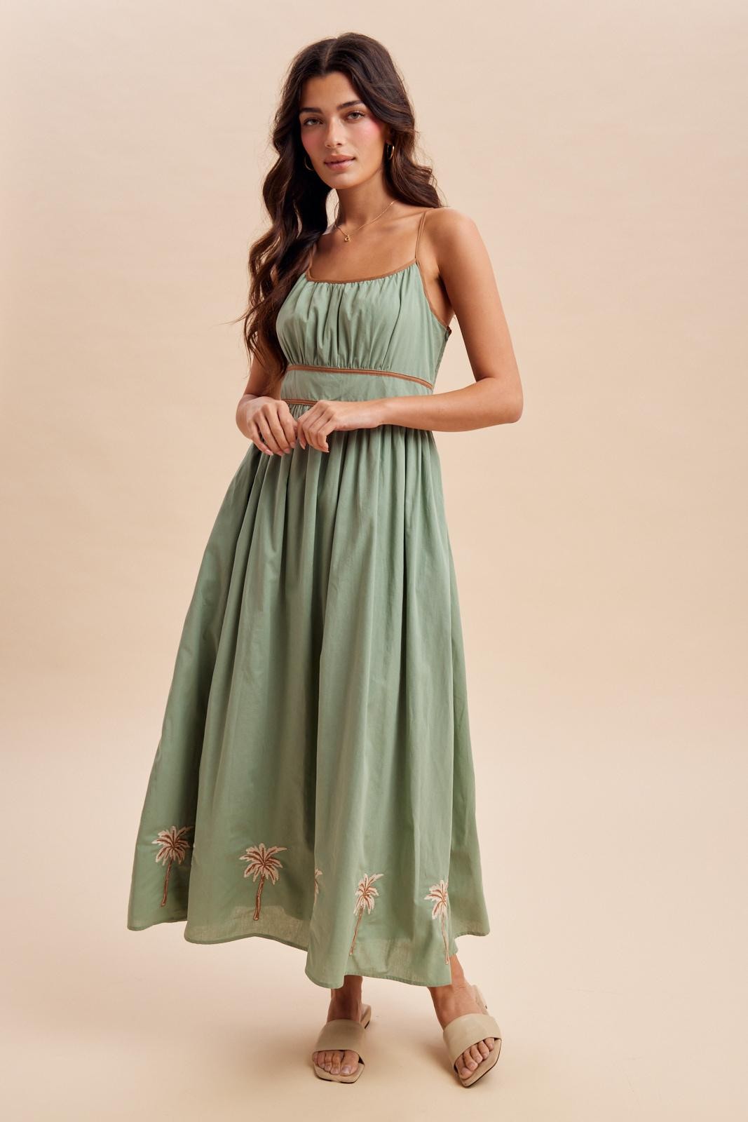 woman wearing a green strapless maxi dress with embroidery at the hem and a fitted bodice