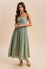 woman wearing a green strapless maxi dress with embroidery at the hem and a fitted bodice