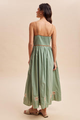 woman wearing a green maxi dress with a smocked bodice and floral embroidery at the hem, shown from the back