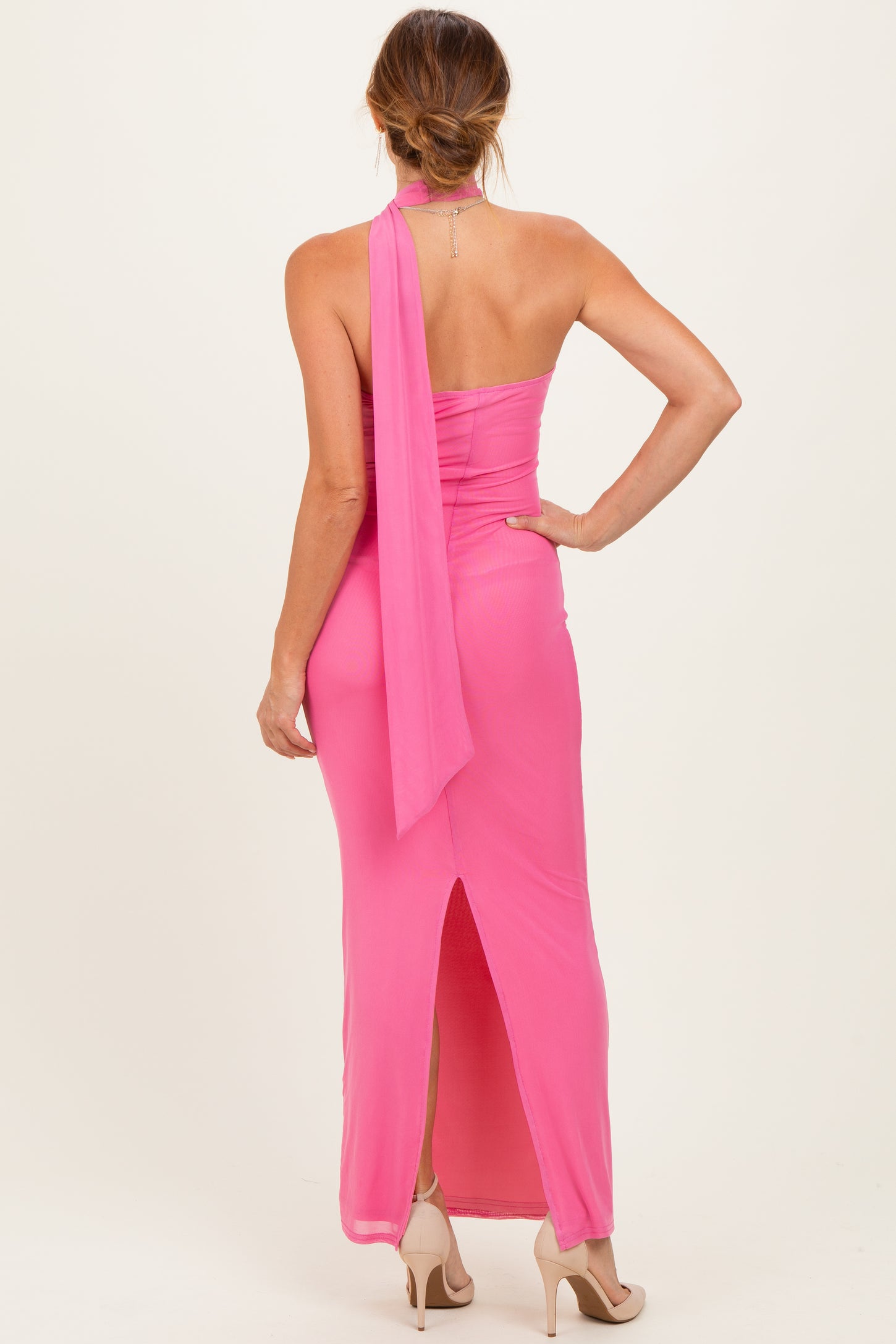 woman wearing a pink halter neck maxi dress with a slit at the back and a flowing scarf detail