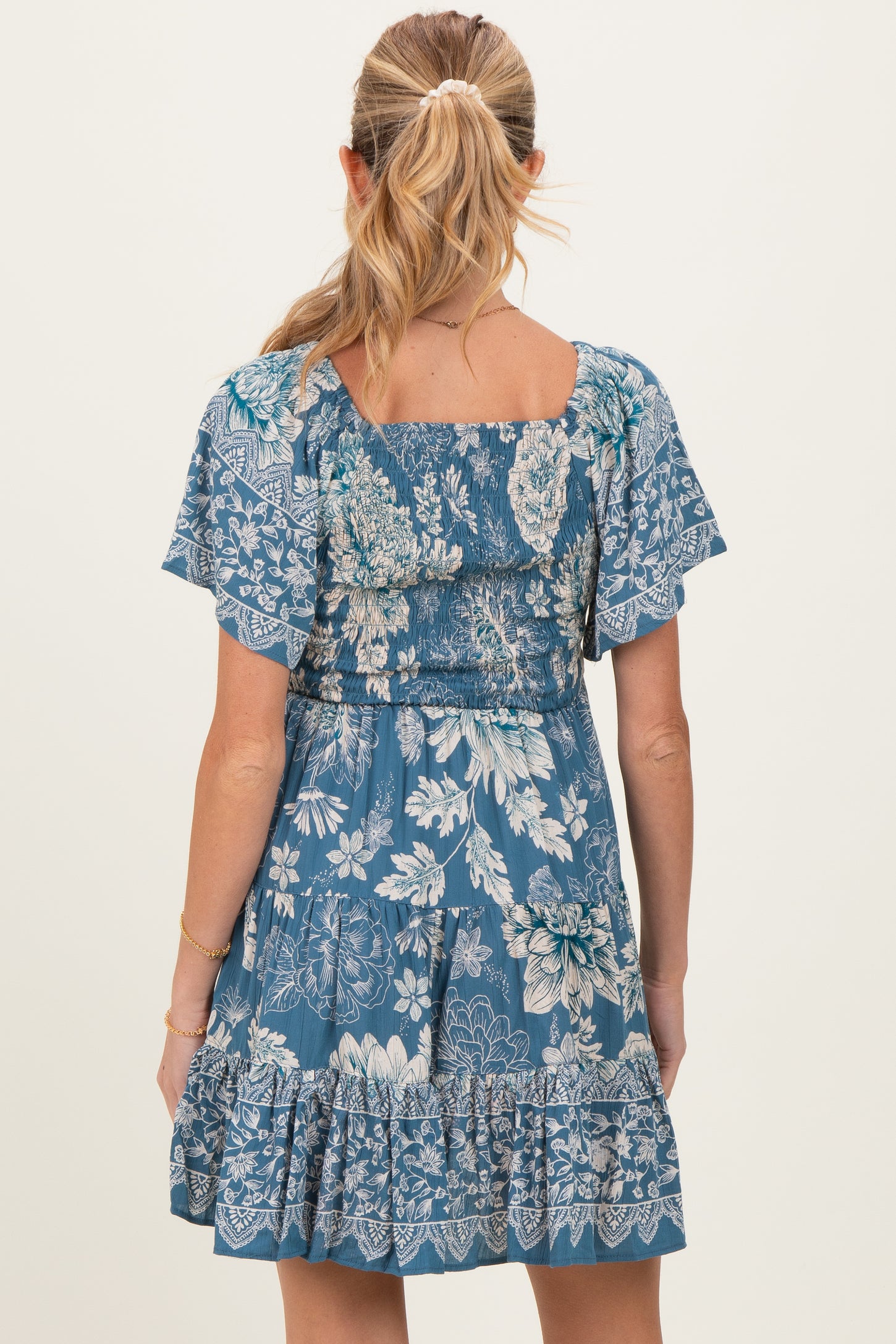 woman wearing a blue floral maternity dress with short flutter sleeves and a ruffled hem, shown from the back
