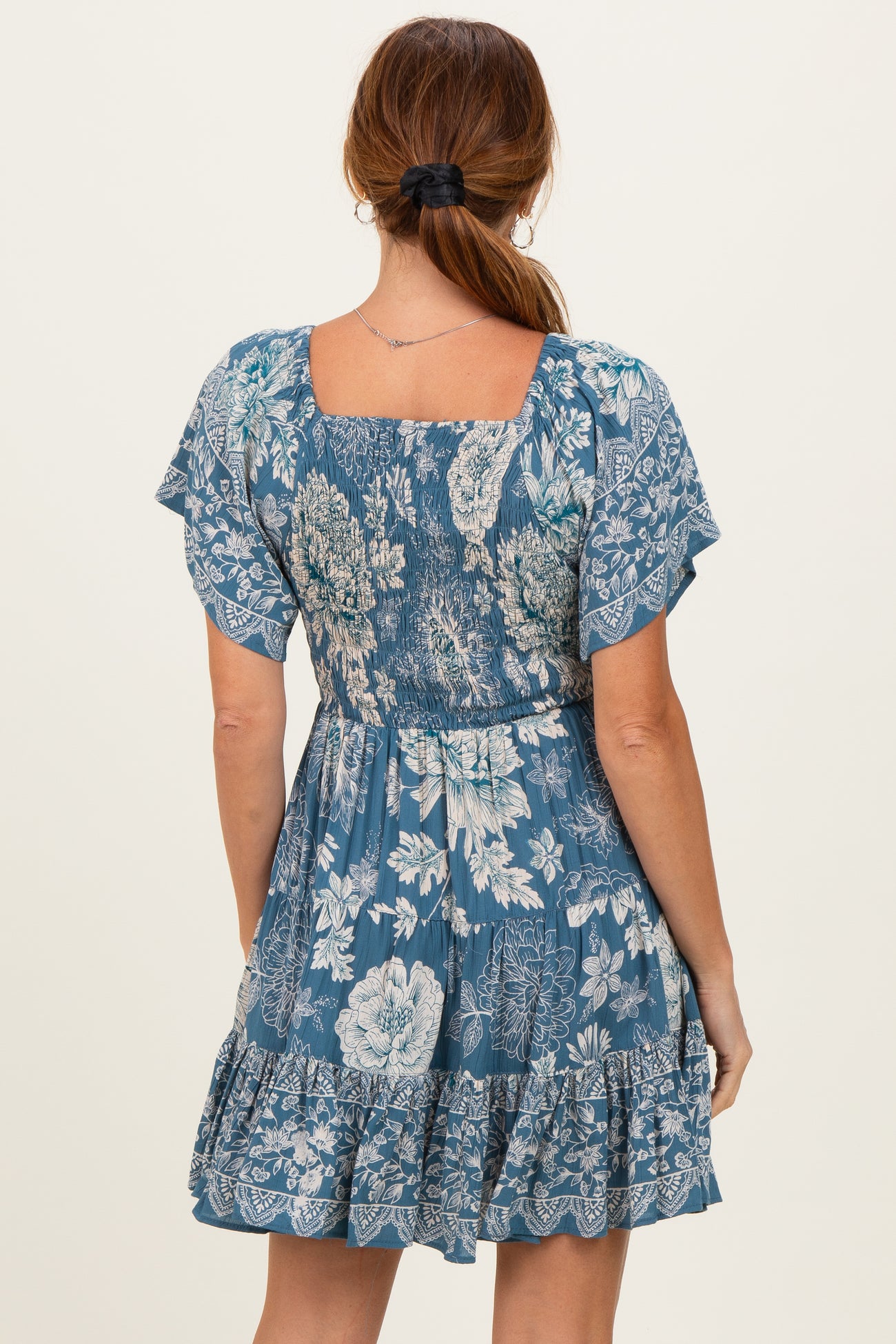 woman wearing a blue floral print dress with short sleeves and a tiered ruffle hem, viewed from the back