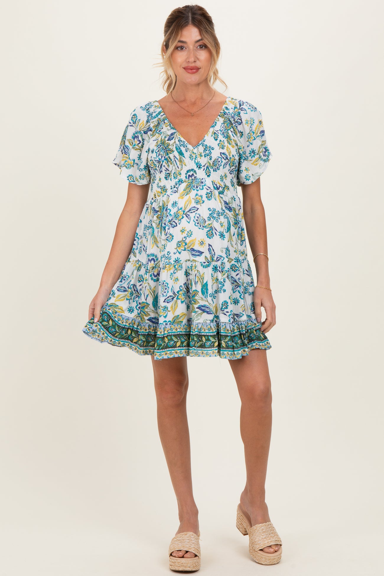 woman wearing a floral print maternity dress with short sleeves and a ruffled hem, showing her baby bump
