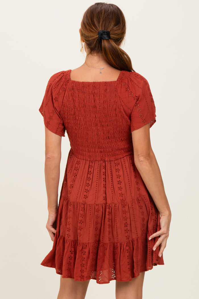 woman wearing a rust-colored short sleeve dress with a smocked bodice and tiered skirt, shown from the back