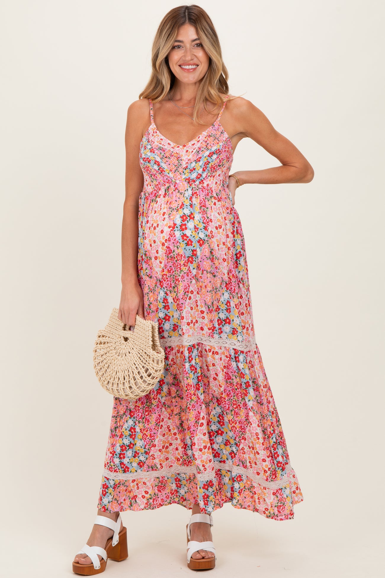 woman wearing a floral maternity maxi dress with adjustable straps and a baby bump, holding a woven bag