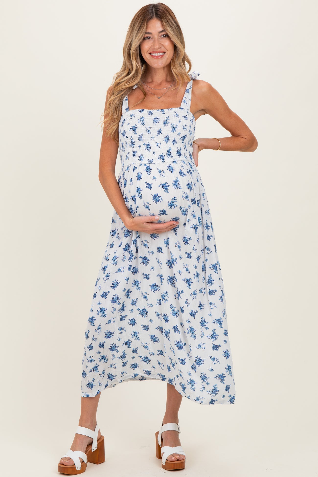 woman wearing a white floral maternity dress with blue flowers, holding her baby bump