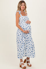 woman wearing a white floral maternity dress with tie straps and holding her baby bump