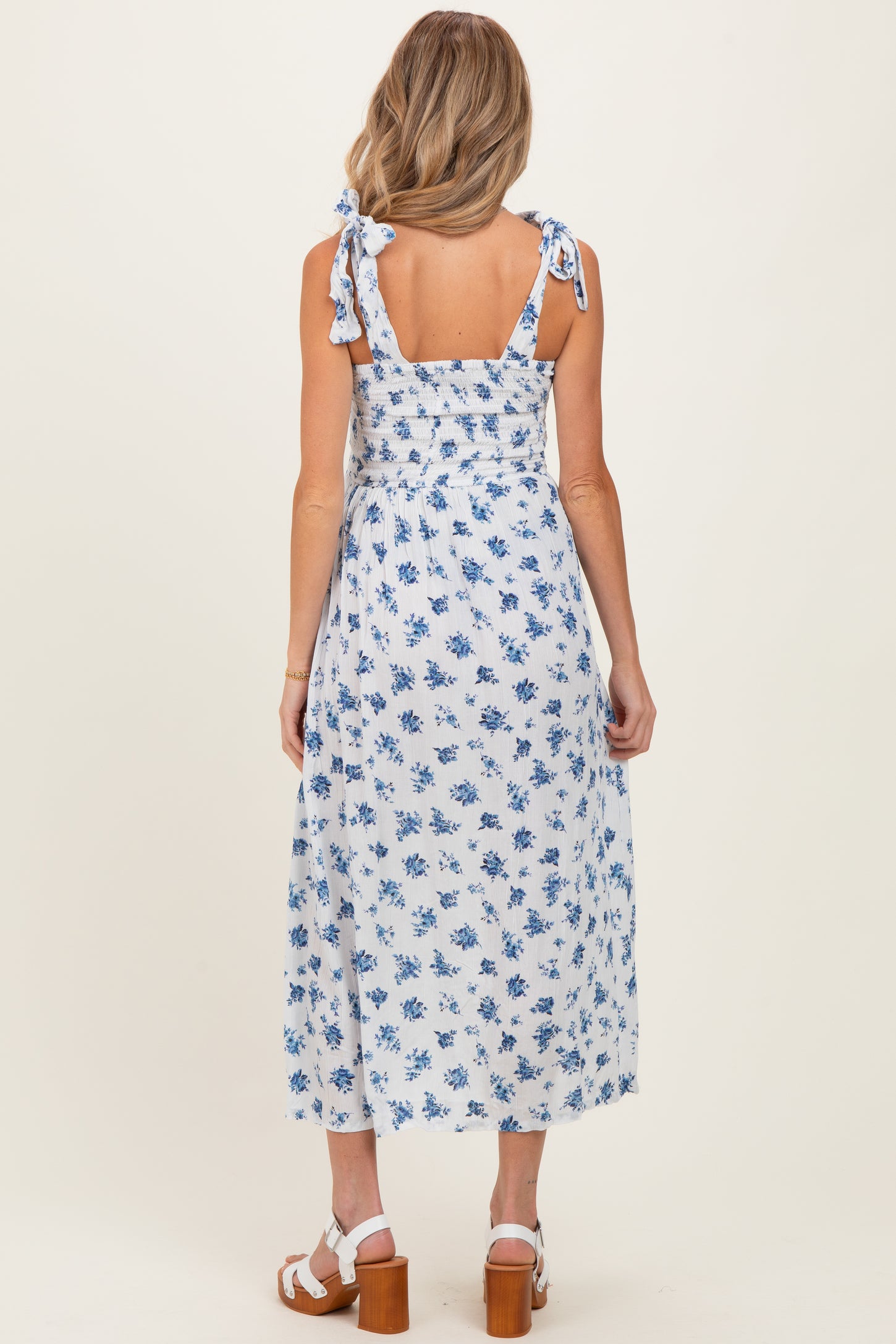 woman wearing a blue and white floral maternity dress with tie straps and a smocked back, showing a baby bump