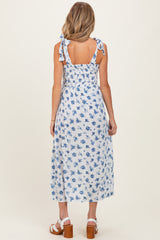 woman wearing a blue and white floral maternity dress with tie straps and a smocked back, showing a baby bump