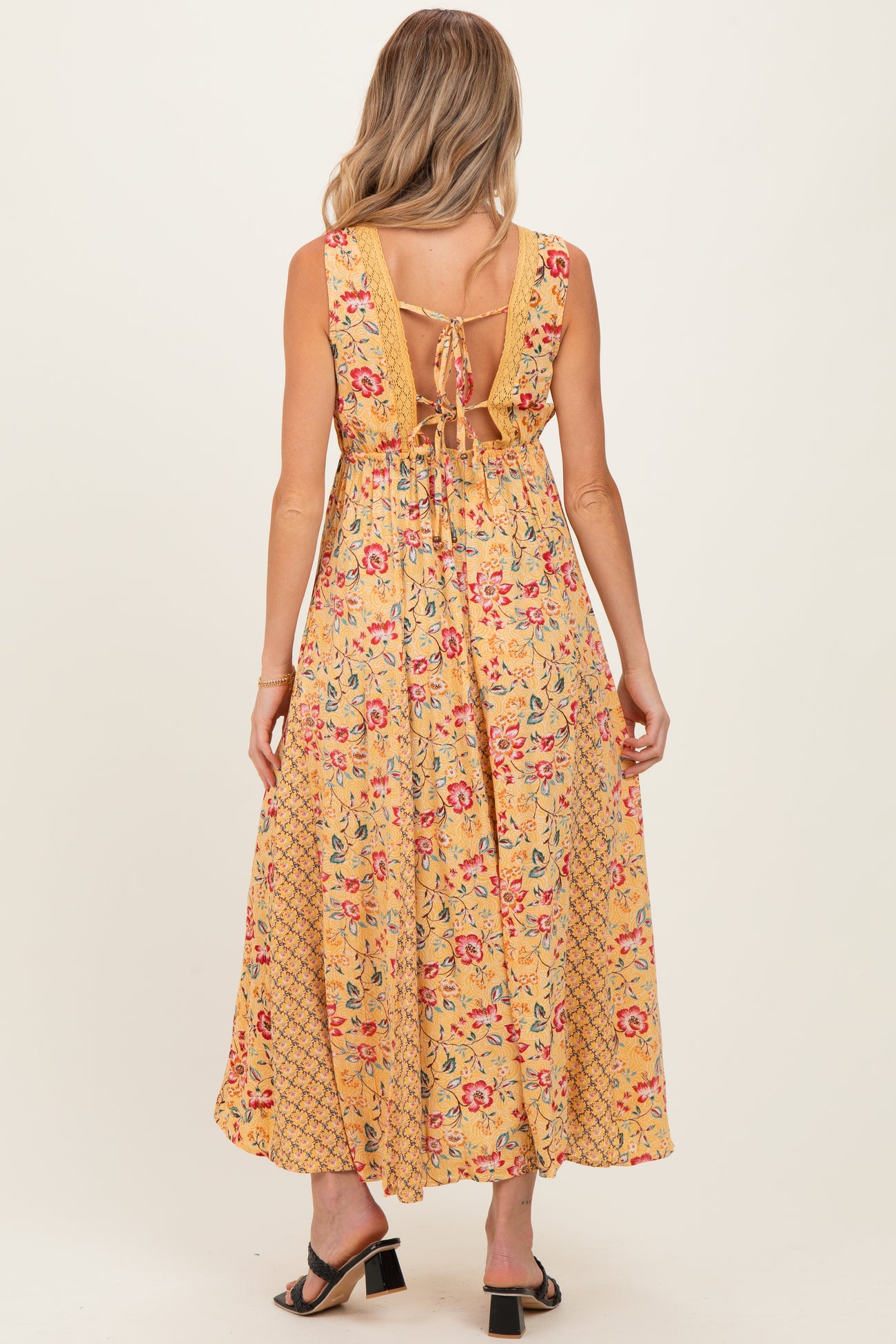 woman wearing a yellow floral maternity maxi dress with a tie back and open back detail, showing style details
