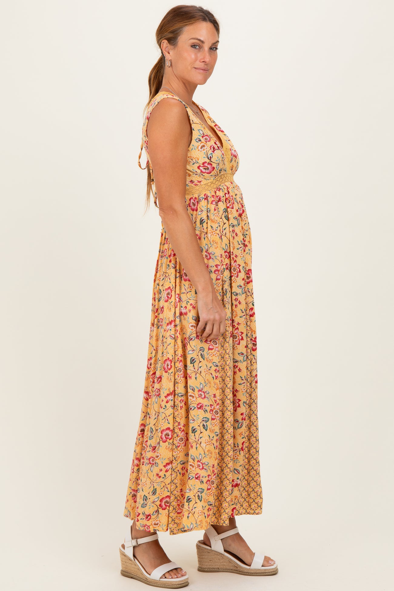 woman wearing a yellow floral maxi dress with a v-neckline and tie straps, standing sideways with a smile