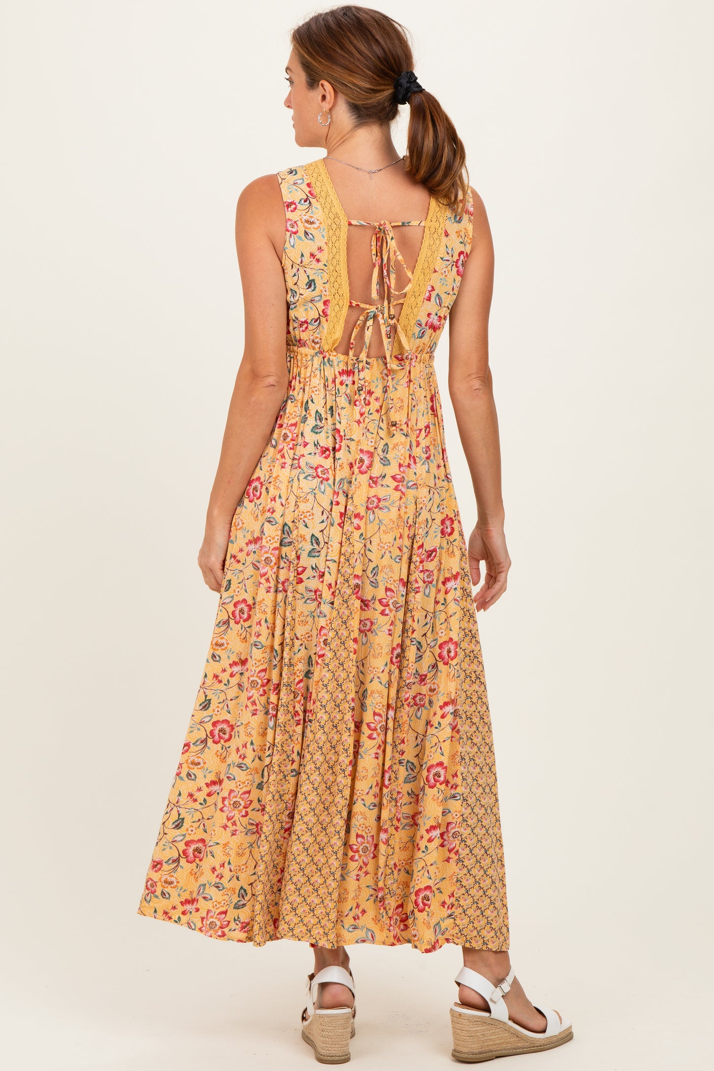 woman wearing a yellow floral maxi dress with a tied back and ruffled detail, styled with wedge sandals