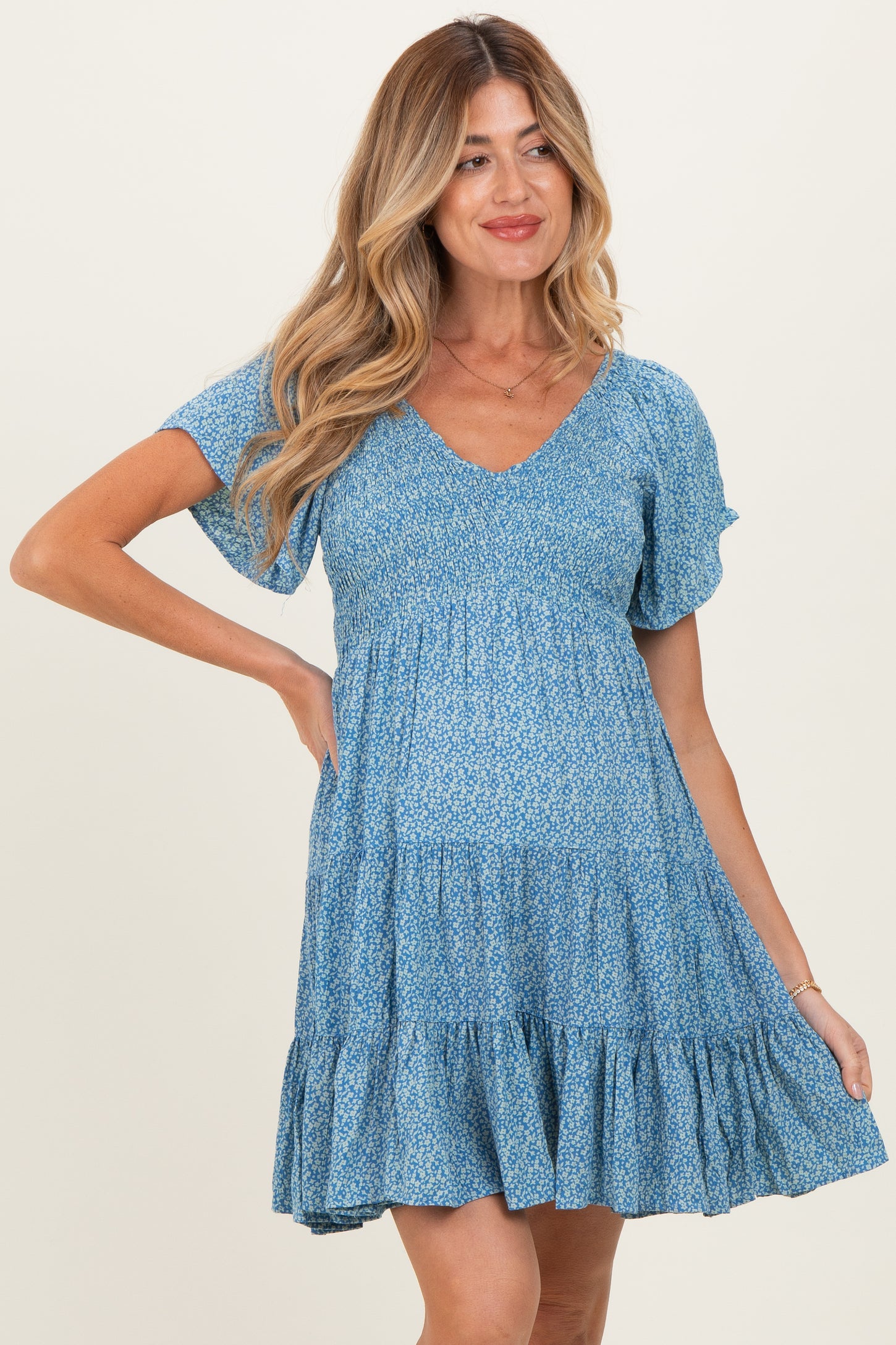 woman wearing a light blue floral maternity dress with short sleeves and a tiered ruffle hem, showing her baby bump